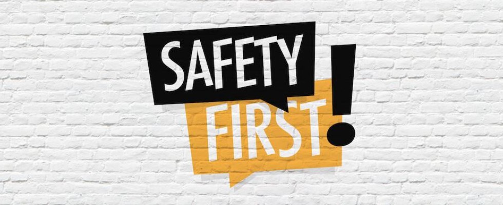 The words "Safety First" in black and orange text bubbles with a blocky exclamation point to the side over a white brick background 