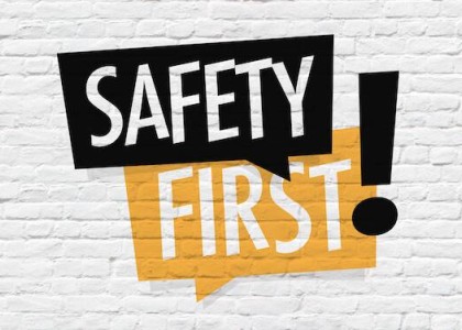 The words "Safety First" in black and orange text bubbles with a blocky exclamation point to the side over a white brick background 