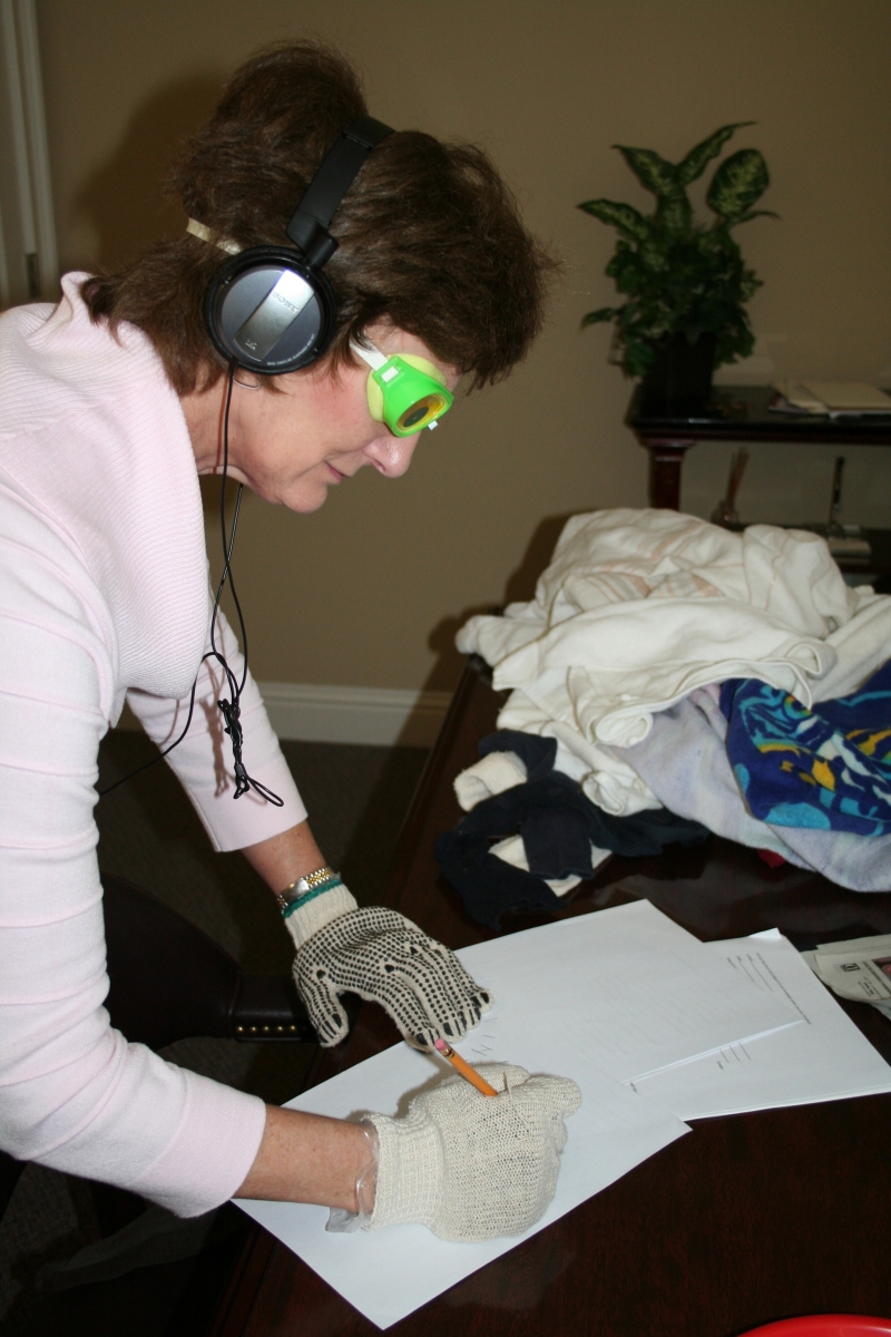 A Virtual Dementia Tour participant attempts to write while wearing gloves that simulate the experience of sensory atrophy.