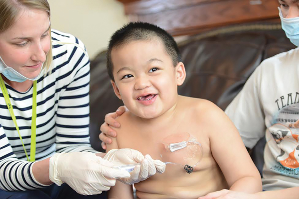 A pediatric home health nurse administers medication through a port