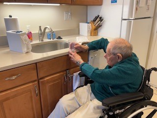 Author's father sitting in wheelchair at kitchen sink, unable to reach faucet or inside sink. 