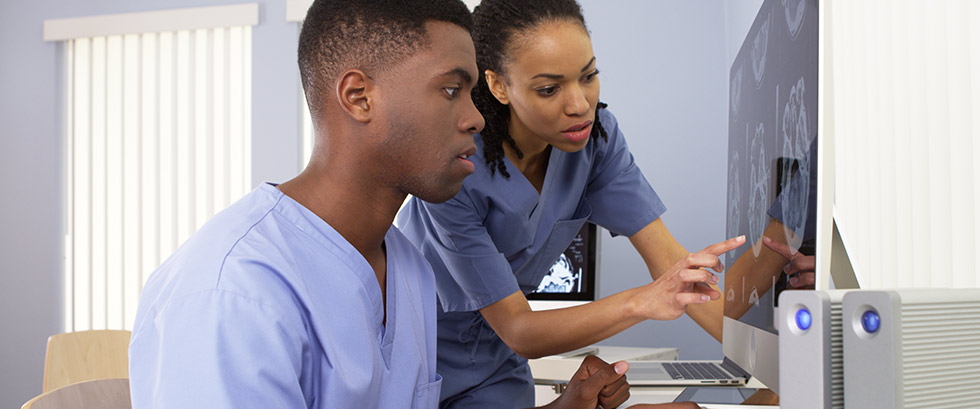 one black male nurse and one black female nurse looking at a computer screen