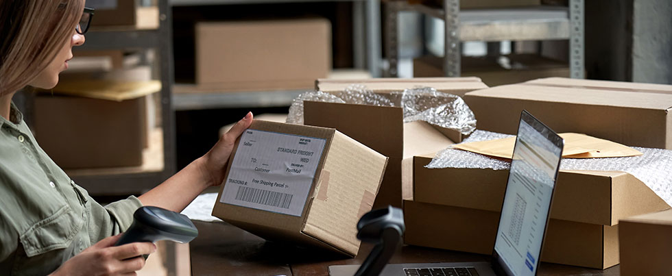 white woman in green shirt scans shipping boxes