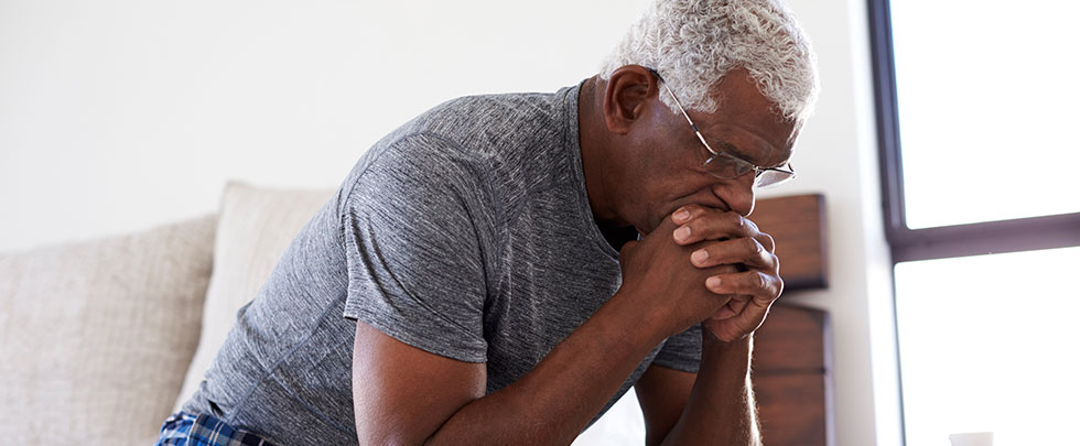 older Black man sits with his chin on his hands looking worried