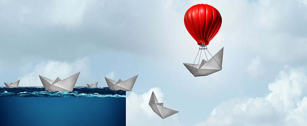 Paper boats falling over a waterfall except for one protected by a red balloon