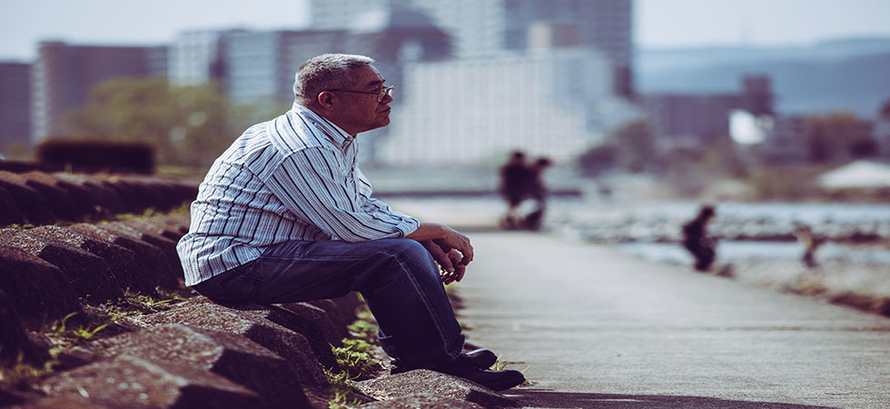 Asian senior adult male sitting alone in a park looking pensive