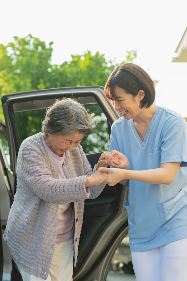 Young health care worker helps senior woman out of a car.  