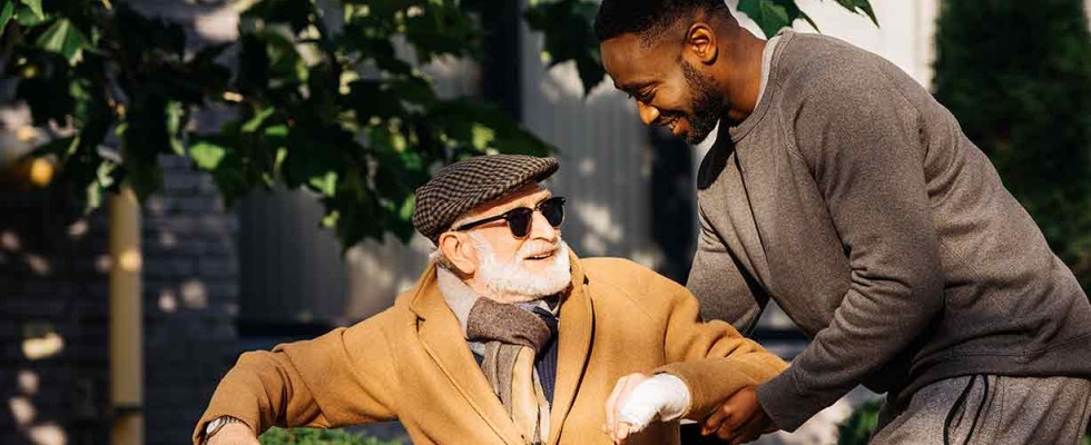 An elderly man in a wheelchair is helped by his caregiver