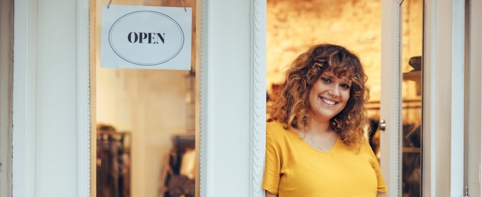 A woman stands in the doors of a boutique that has an "open" sign on the door. 