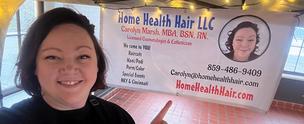 Carolyn Marsh standing next to her Home Health Hair LLC banner