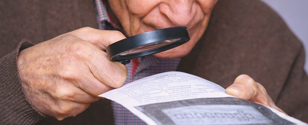 older white man using a magnifying glass to read a piece of paper