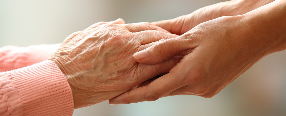 An up-close image of two people clasping hands. One set of hands is elderly and one set is a younger adults. 