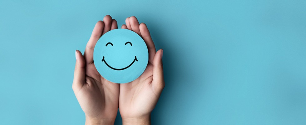 An image of hand against a blue background holding a blue circle smiley face