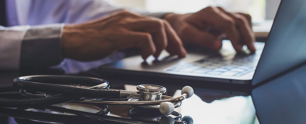 Stethoscope and hands on a computer keyboard 