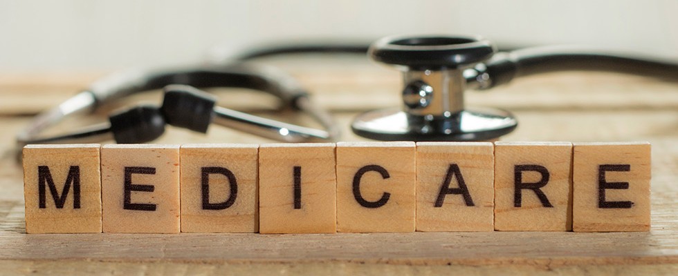 Scrabble pieces spelling out "Medicare" sit on a table, standing up, with a stethoscope behind them. 