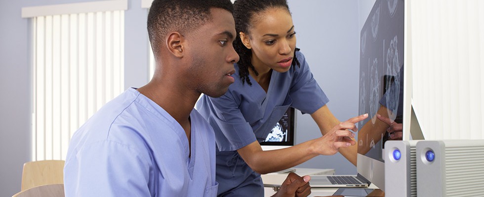 one black male nurse and one black female nurse looking at a computer screen