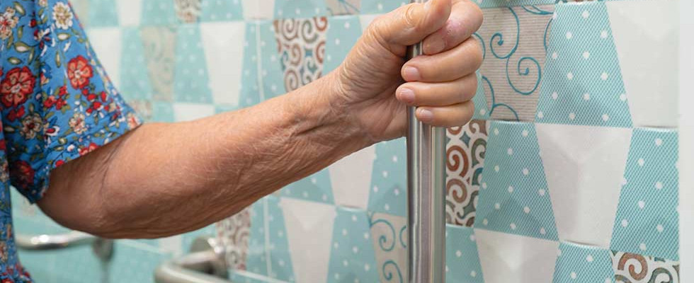 An elderly person holding onto a bath rail.