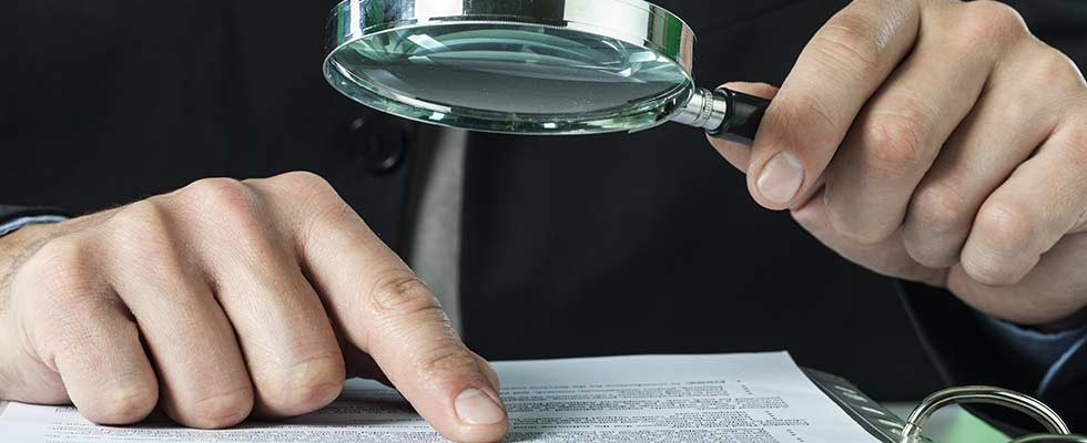 white male hand pointing to legal copy and holding a magnifying glass looking for loopholes