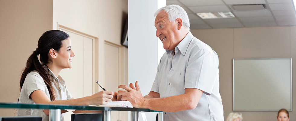 A front of desk person discussing paperwork with an older male patient