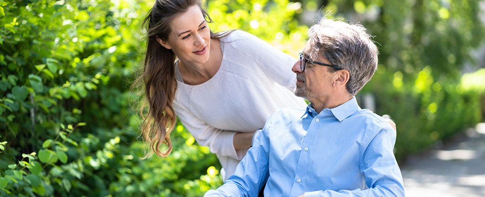 Young white woman smiles at older white man in wheelchair