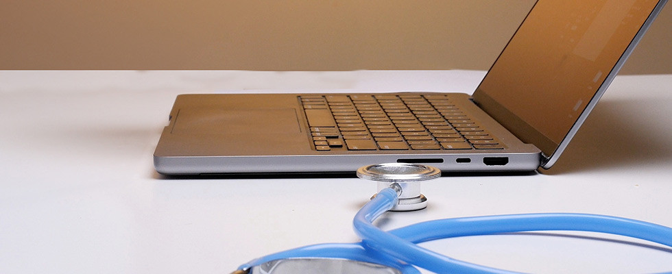 An open laptop sitting on a table next to a stethoscope.