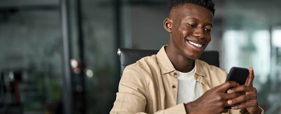 A young man smiles while looking at his cell phone.