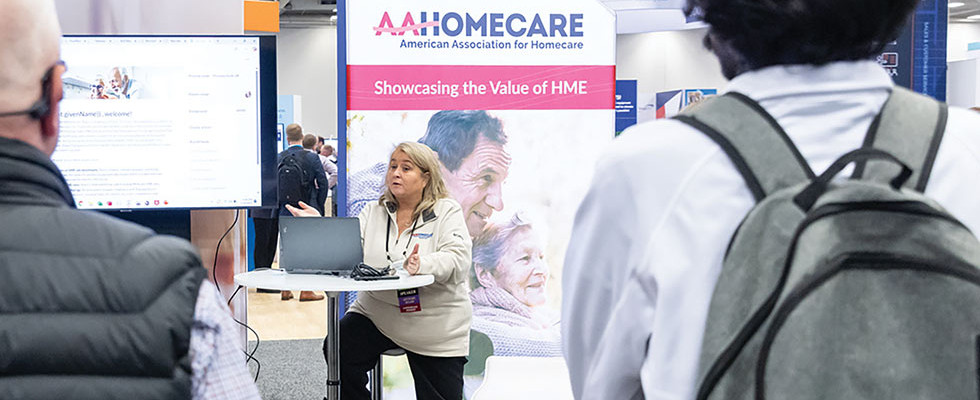 A speaker making a lecture at Medtrade in front of an AAHomecare sign