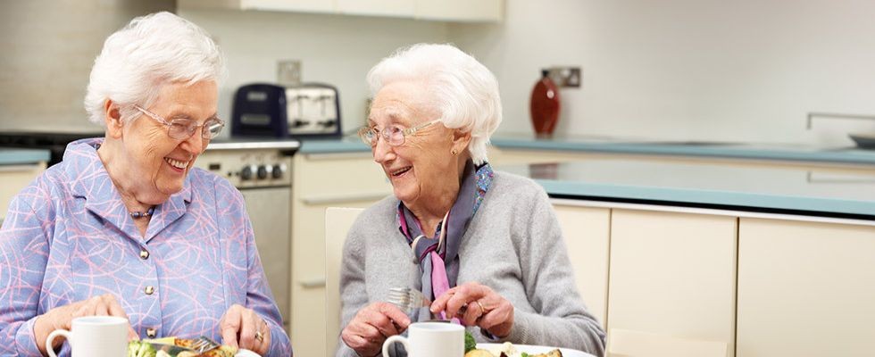 Two elderly women sit and laugh while enjoying their lunch.