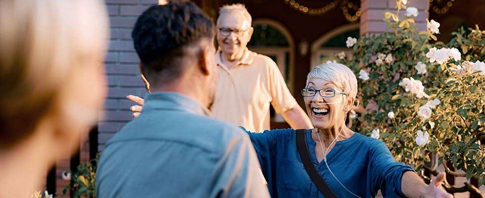A patient wearing a portable oxygen mask smiling with their arms open to hug someone