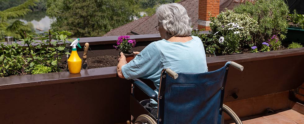 An elderly woman sitting in a wheelchair overlooking a small garden