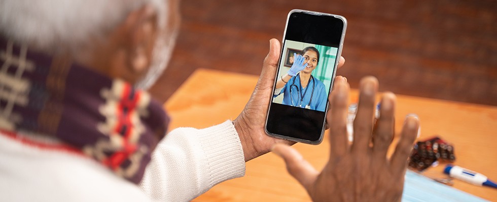 Older Black person using a smartphone for a telehealth appointment. The smartphone screen features a young woman of color in scrubs.