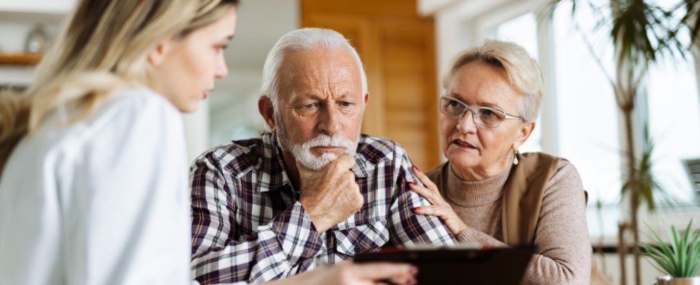 Husband and wife sit with a caregiver looking at a care plan