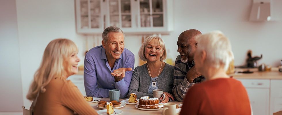 Group of older individuals sitting and laughing while eating cake