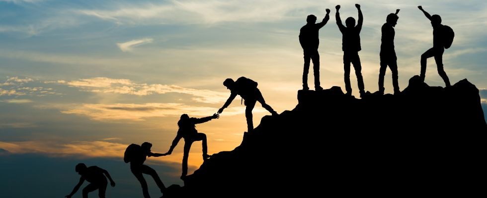 a group of people climbing up a mountain and helping each other reach the top