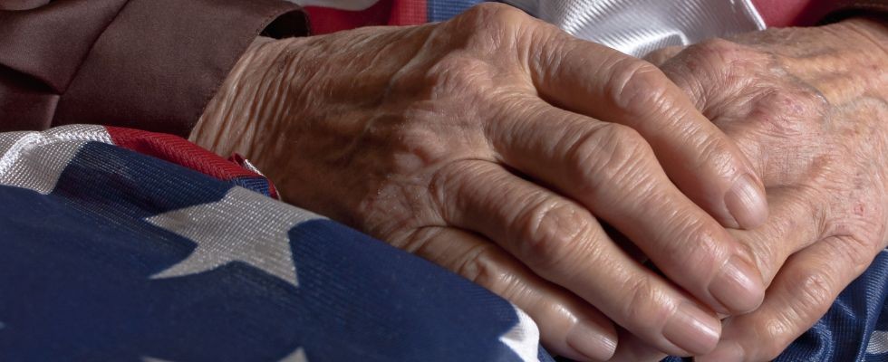 An elderly person's hands clasped over an American flag. 