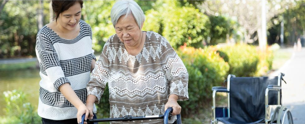 A younger caregiver helping her elderly patient with a walker