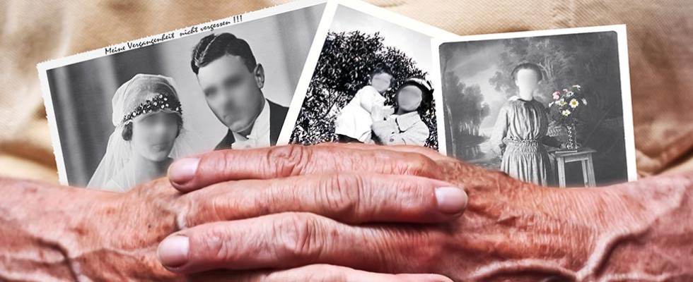 Two elderly hands hold old photographs with the faces blurred out.