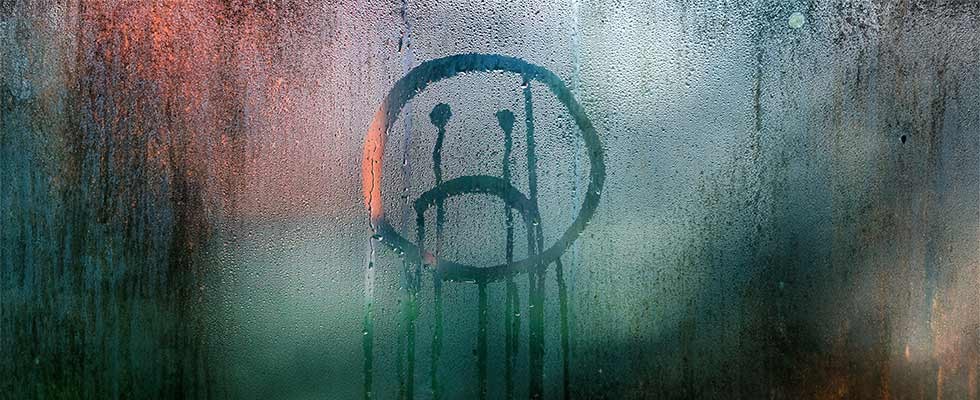a frown face drawn on a window through condensation