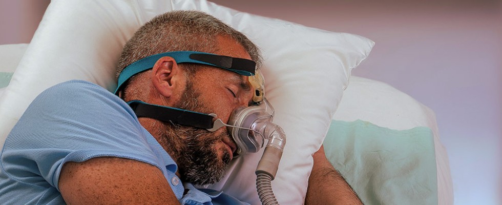 A man sleeps on a pillow with a sleep apnea mask on his face.