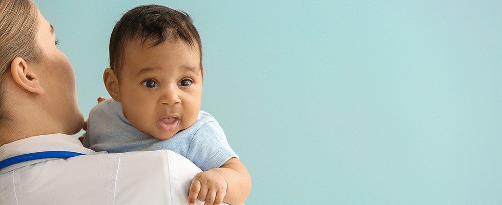 A doctor holds a baby over her shoulder.