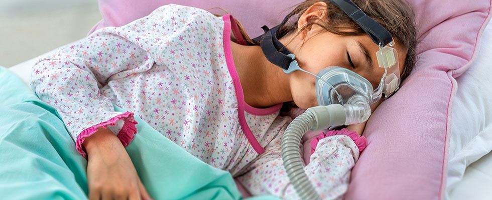 A girl lays sleeping with a CPAP machine on her face