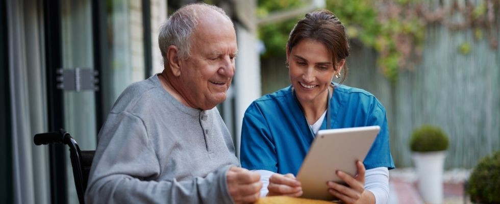 an older man in a wheelchair with a homecare care coordinator looking at an ipad outside