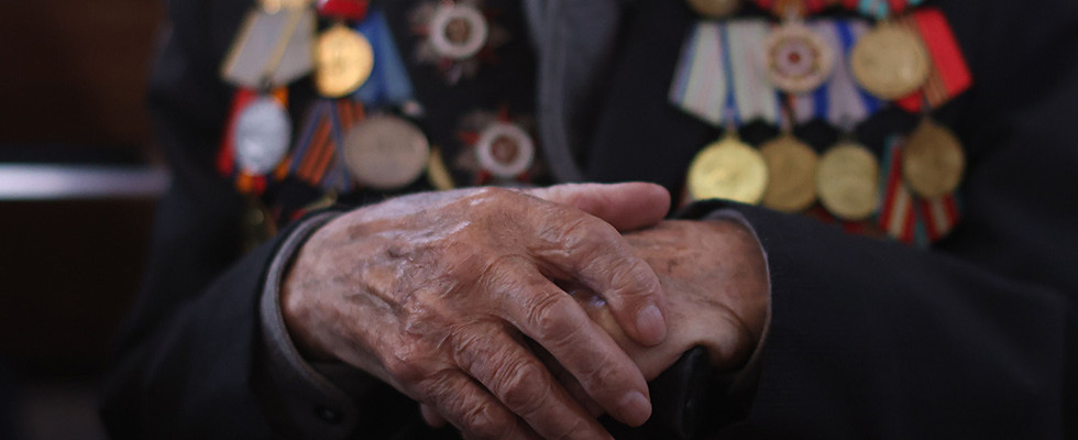 The hands of an elderly person wearing several war medals.