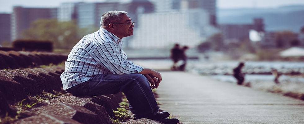 Asian senior adult male sitting alone in a park looking pensive