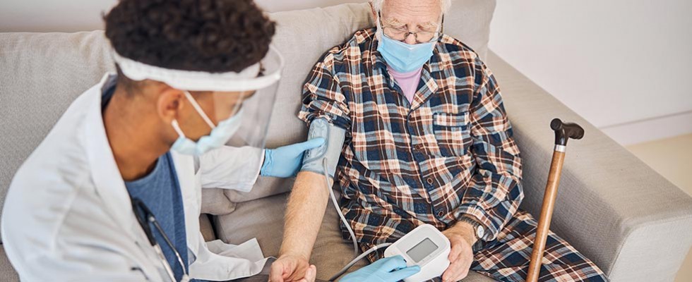 back male nurse in PPE checking blood pressure of older white male