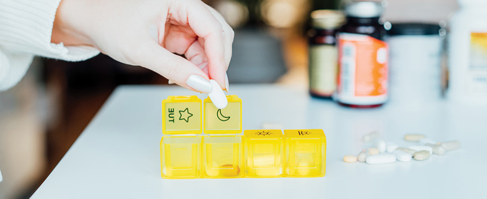 A hand organizing medicine into a pill organizer.