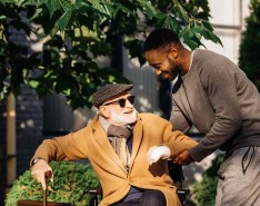An elderly man in a wheelchair is helped by his caregiver