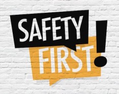 The words "Safety First" in black and orange text bubbles with a blocky exclamation point to the side over a white brick background 