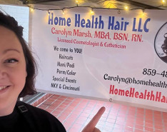 Carolyn Marsh standing next to her Home Health Hair LLC banner
