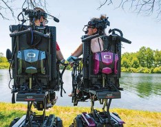 Two people sitting in medical assist chairs by a sunny lake